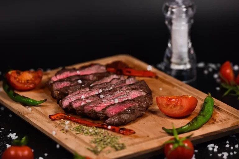 Juicy grilled Coulotte steak sliced on a wooden cutting board, garnished with fresh herbs and served with roasted vegetables and a side of chimichurri sauce.
